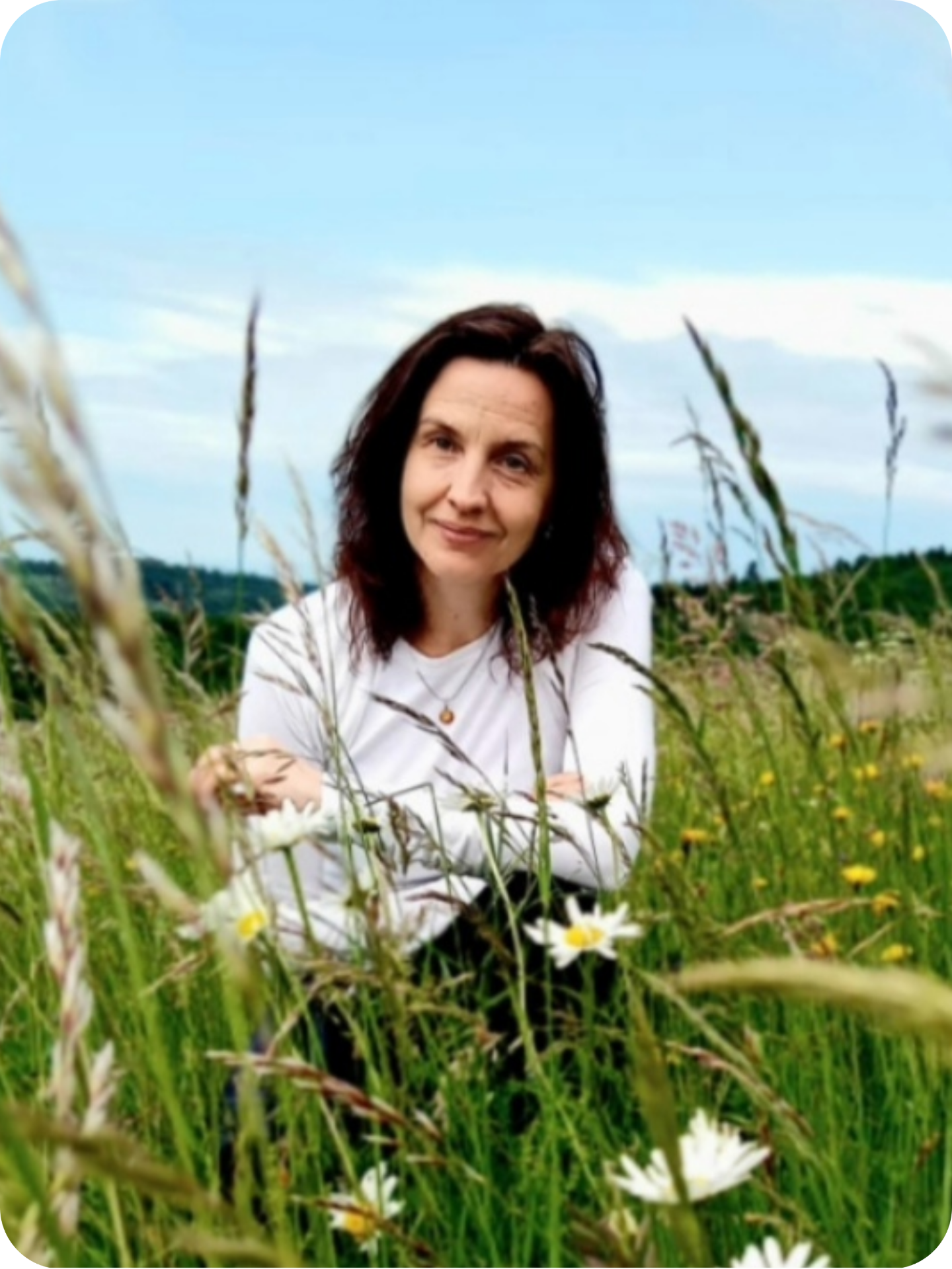 Žena, poradkyně Eva Prokešová, v bílém tričku sedí v louce mezi květy, usmívá se proti obloze a užívá si vnitřní klid.